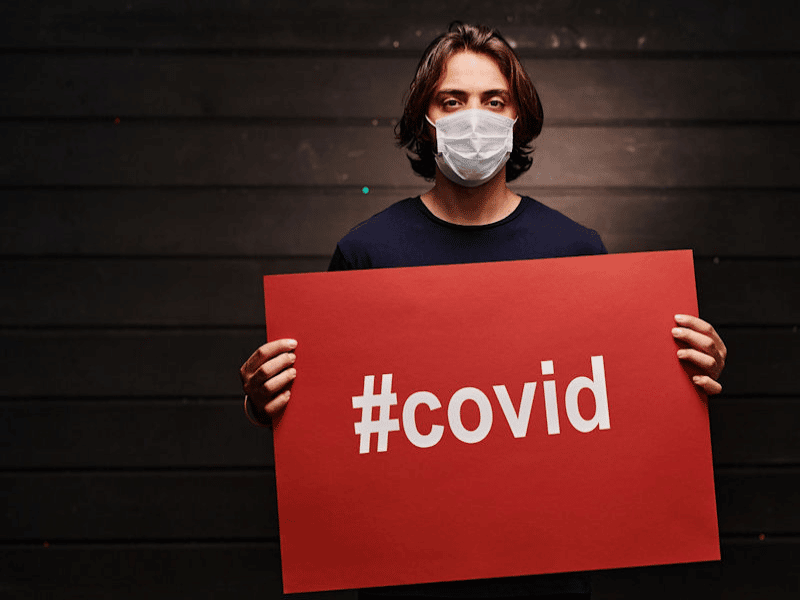 Masked man holding sign that says #covid.