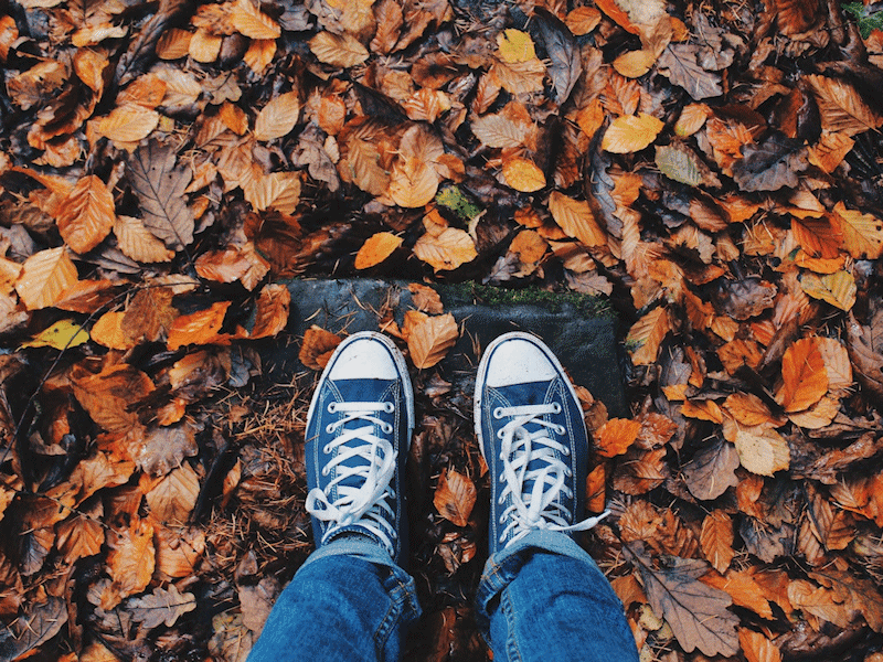 Person in jeans and blue casual shoes standing on autumn leaves, illustrating seasonal affective disorder.