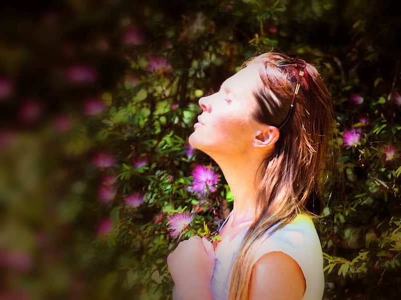 Woman in garden, smelling flowers and practicing mindfulness.