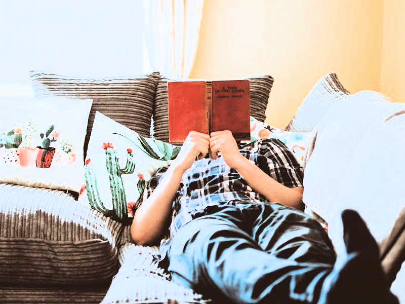 A man lying on a sofa, reading.