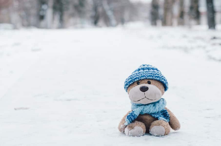 Teddy bear dressed in blue hat and scarf sitting in the snow.